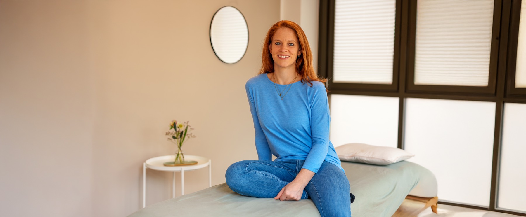 Kathrin Pesch sitzt lächelnd auf der Behandlungsliege in ihrer Praxis in Köln